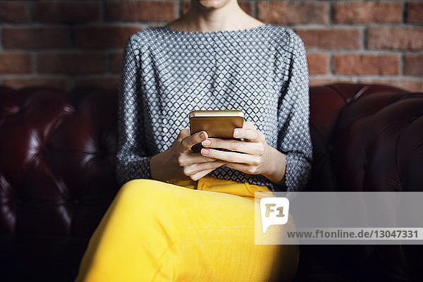 Midsection of businesswoman using smart phone on couch at office lobby