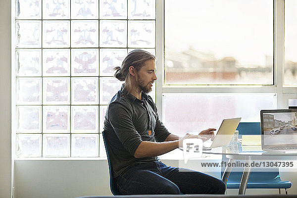 Geschäftsmann mit Laptop auf Tisch gegen Fenster im Kreativbüro