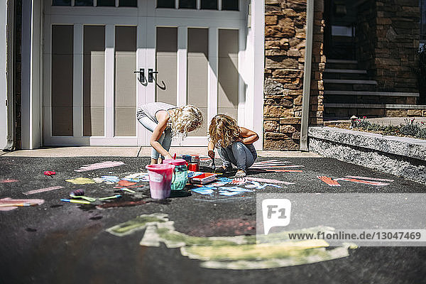 Verspielte Schwestern malen bei Sonnenschein auf Asphalt vor dem Haus