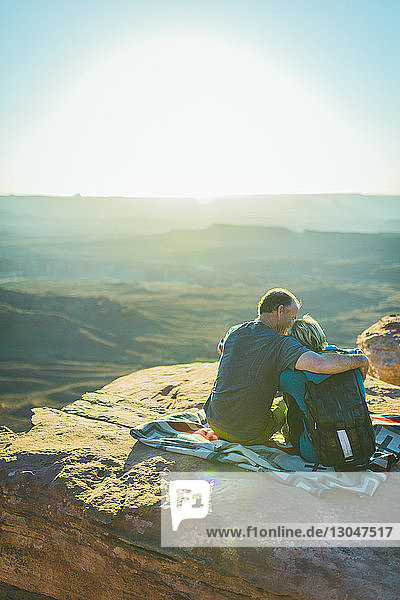 Rückansicht eines romantischen Paares  das an einem sonnigen Tag im Canyonlands-Nationalpark auf einem Berg sitzt