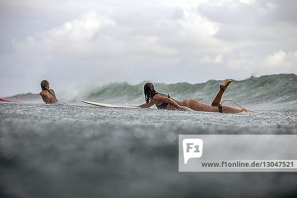 Freunde auf dem Surfbrett liegend beim Surfen im Meer während der Regenzeit