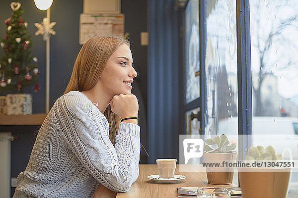 Side view of thoughtful woman with hand on chin sitting at table in cafe during Christmas