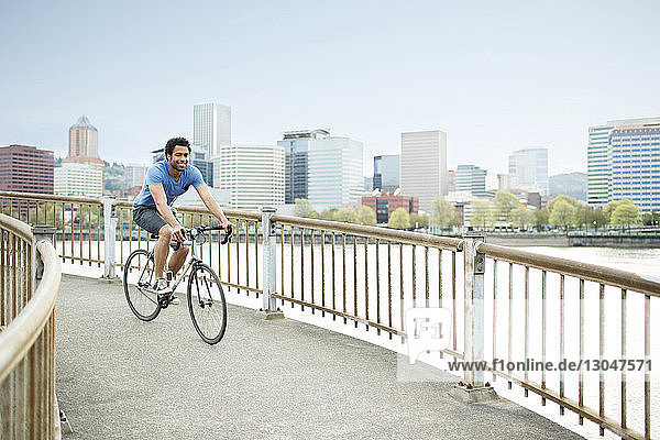 Junger männlicher Athlet beim Fahrradfahren auf einer Brücke am Fluss in der Stadt