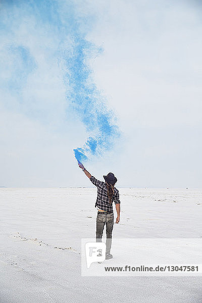 Rear view of man holding smoke bomb while standing on Bonneville Salt Flats against sky