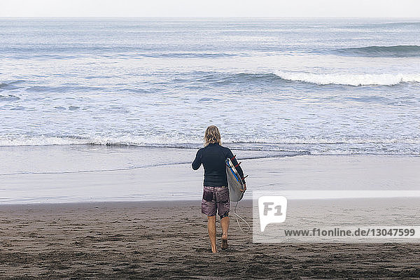 Hochwinkelansicht eines Mannes  der ein Surfbrett trägt  während er am Strand in Richtung Meer läuft