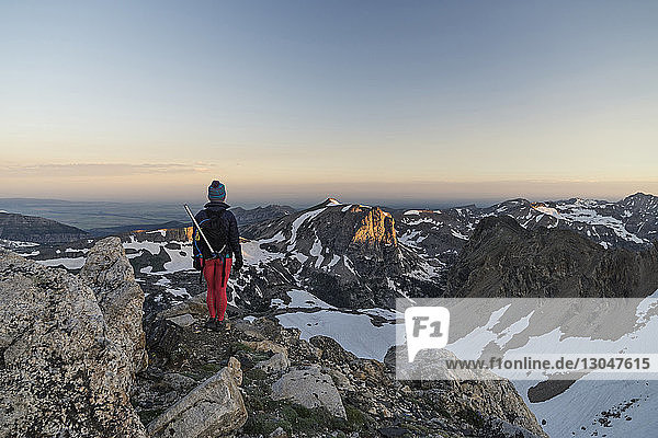 Rear view of hiker standing on mountain against sky during sunset