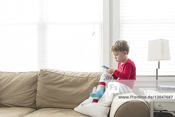 Side view of boy using mobile phone while sitting on sofa at home