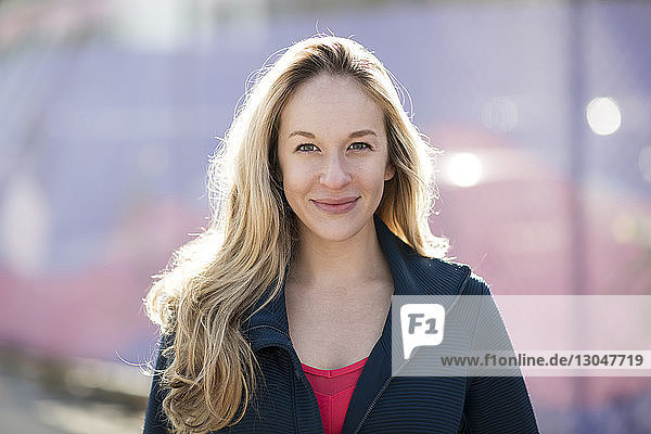 Close-up portrait of confident athlete standing by fence during sunny day