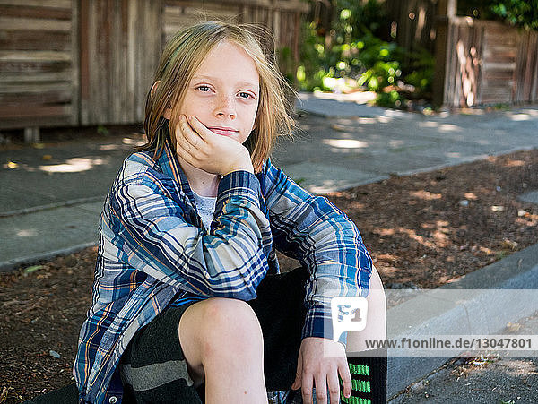 Portrait of confident boy sitting on footpath