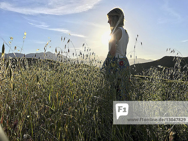 Seitenansicht einer Frau  die im Sommer auf einem Grasfeld gegen den Himmel steht