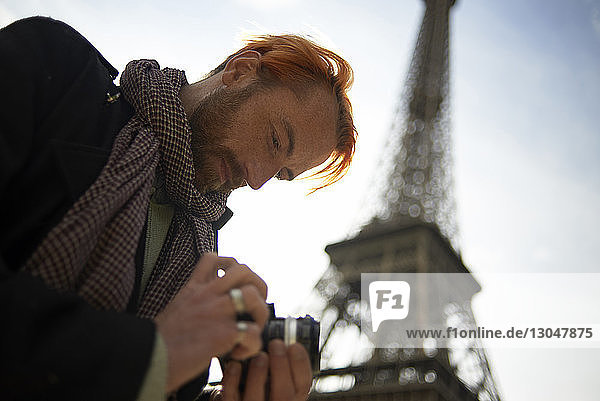 Low angle view of man watching pictures on DSLR camera against Eiffel Tower