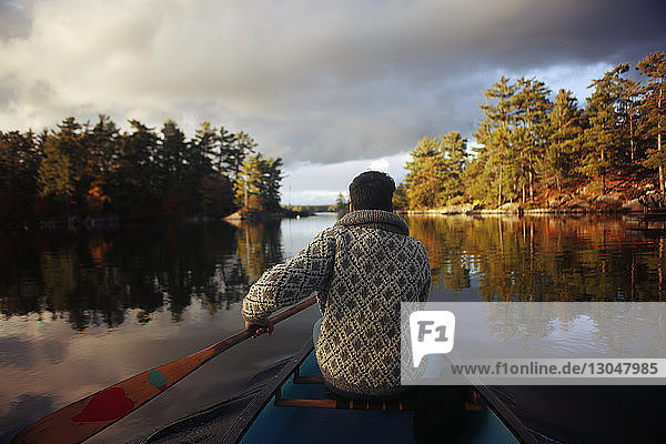 Rear view of man canoeing on lake against cloudy sky during sunset