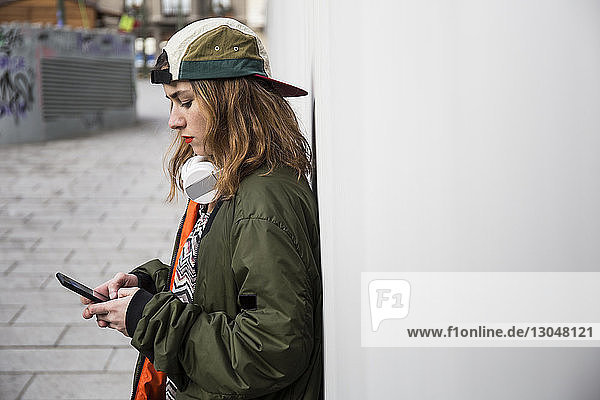 Seitenansicht einer Frau  die ein Smartphone benutzt  während sie an der Wand steht