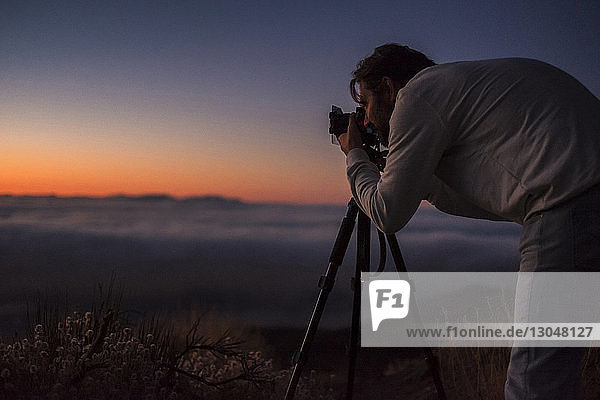Seitenansicht eines Mannes  der bei Sonnenuntergang mit der Kamera gegen den Himmel fotografiert