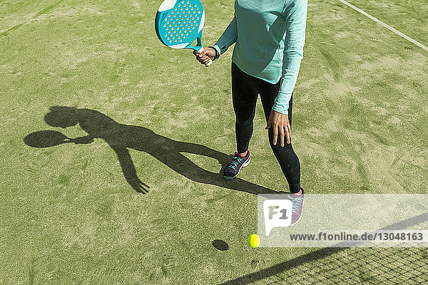 Niedriger Abschnitt einer Frau,  die bei Sonnenschein Paddle-Tennis auf dem Platz spielt