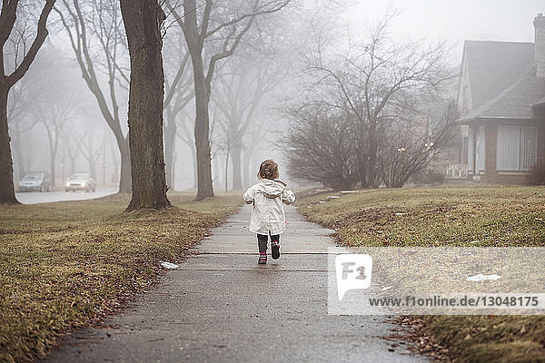 Rückansicht eines Mädchens in Regenmantel beim Gehen auf einem Fußweg bei nebligem Wetter