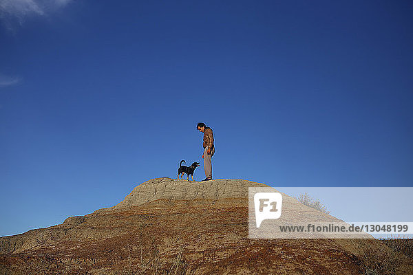 Low angle view of man standing with dog on mountain against blue sky