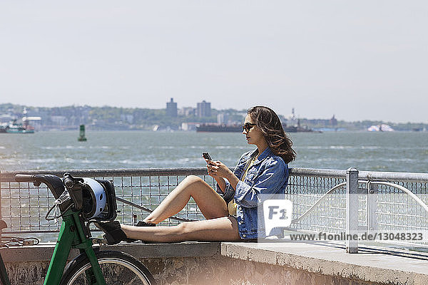 Frau benutzt ein Smartphone  während sie auf der Stützmauer am Beobachtungspunkt sitzt