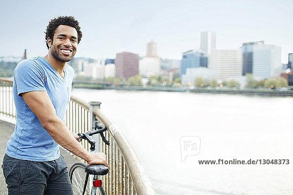 Portrait of male athlete standing on bridge with bicycle by river