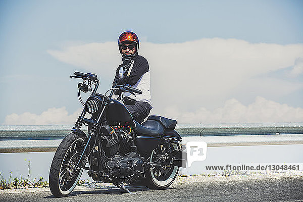 Biker standing by cruiser motorcycle on roadside against sky