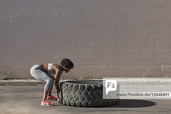 Side view of woman lifting tire truck while exercising against wall