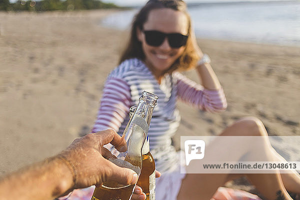 Abgehackte Hand eines Mannes  der mit einem Freund am Strand auf Bier anstößt