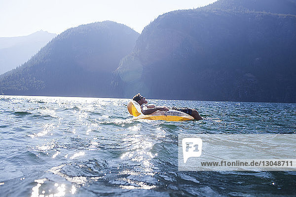 Seitenansicht eines Mannes  der im Sommer auf einem Floß im See vor den Bergen liegt