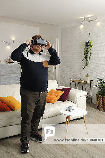 Mann schaut zu Hause durch einen Virtual-Reality-Simulator  während er zu Hause steht