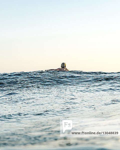 Rückansicht einer im Meer schwimmenden Frau vor klarem Himmel