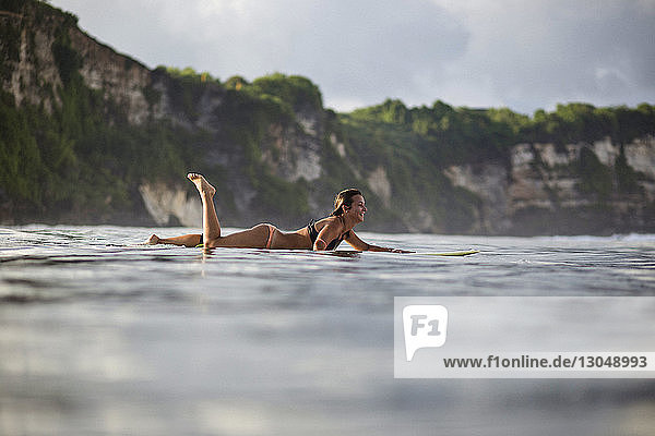Glückliche Frau liegt auf einem Surfbrett am Strand gegen den Himmel