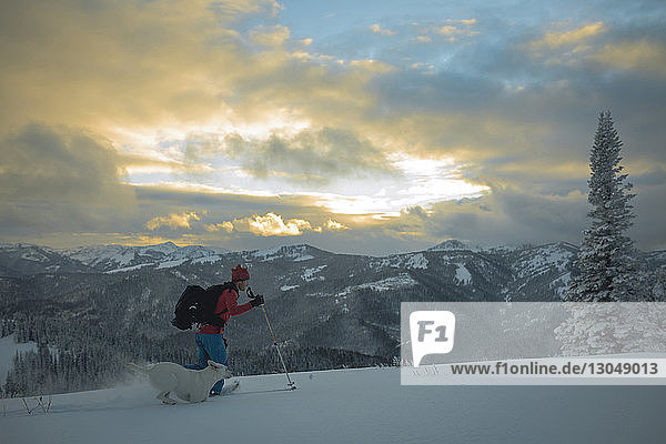 Seitenansicht eines Mannes mit Hund beim Skifahren auf einem schneebedeckten Feld