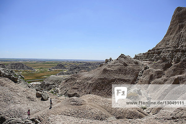 Distant view of siblings hiking at Badlands National Park against clear sky