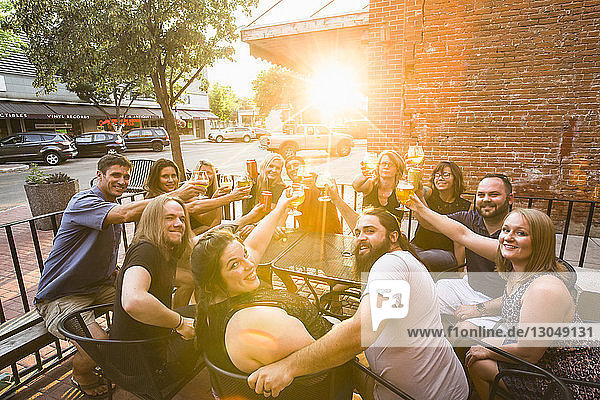 Porträt von glücklichen Freunden  die bei sonnigem Wetter im Straßencafé sitzen und auf Bier anstoßen