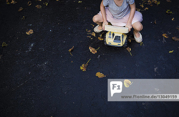 Low section of playful girl driving toy car on road
