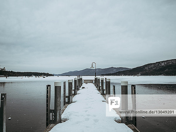 Schneebedeckter Pier über dem zugefrorenen Lake George vor bewölktem Himmel