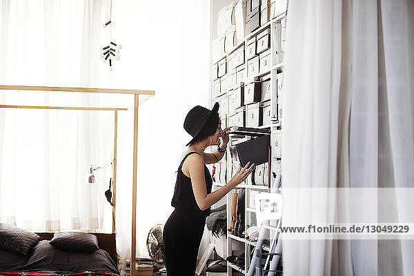 Side view of happy woman searching in box by shelves in bedroom