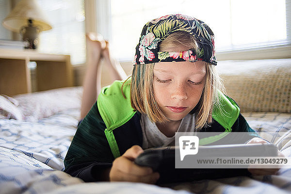 Boy using tablet computer while lying on bed at home