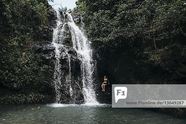 Frau sitzt auf einem Felsen am Wasserfall im Wald