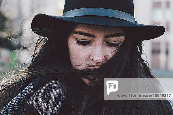 Close-up of thoughtful young woman wearing hat in city