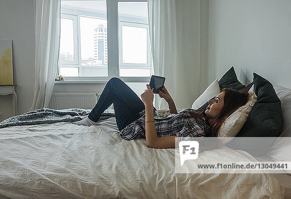 Teenager-Mädchen liegt im Bett  während sie zu Hause einen Tablet-Computer benutzt
