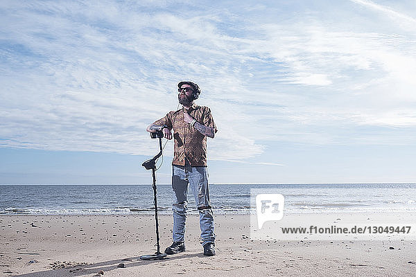 Mann in voller Länge schaut weg  während er den Arm auf dem Metalldetektor am Strand von Horsey Beach ausruht