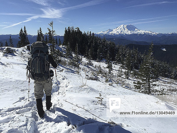 Rückansicht eines Mannes mit Rucksack und Skistöcken beim Gehen auf schneebedecktem Feld