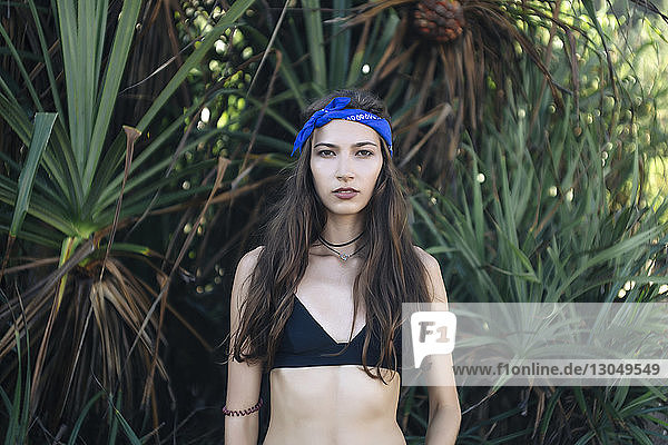 Portrait of confident woman wearing bandana and bikini while standing against plants