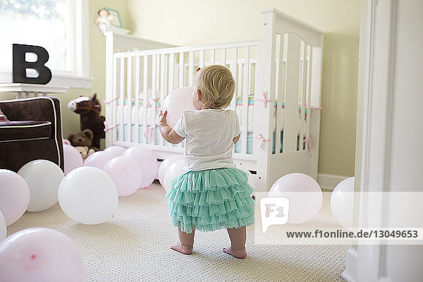 Rückansicht eines kleinen Mädchens  das zu Hause mit Luftballons spielt