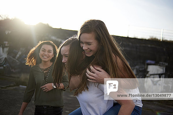 Glückliche Teenagerin schaut Freunden bei Sonnenschein huckepack zu