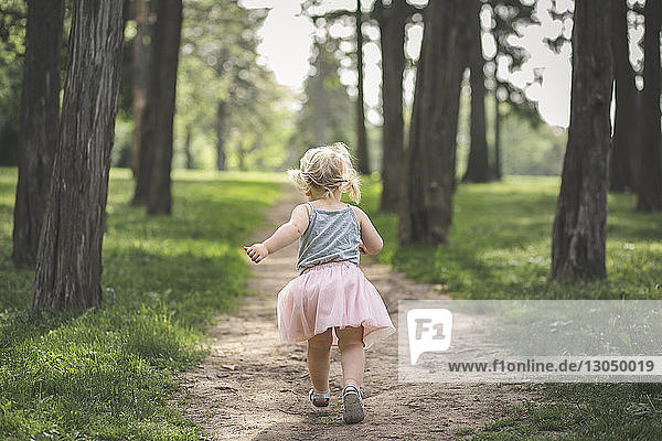 Rear view of girl running on footpath amidst trees at park