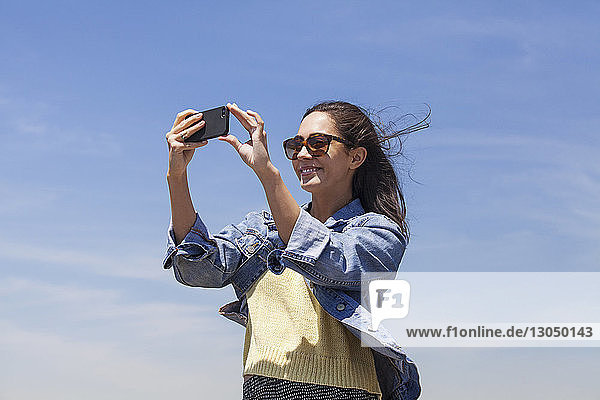 Niedrigwinkelansicht einer schönen Frau  die durch ein Smartphone gegen den Himmel fotografiert