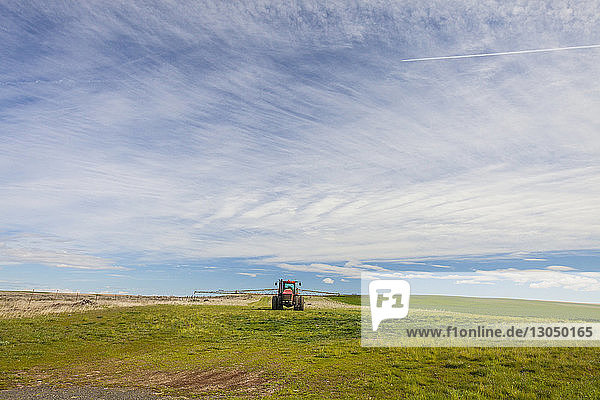 Truck on agricultural landscape against cloudy sky