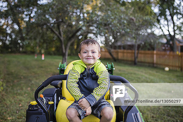 Porträt eines lächelnden Jungen,  der auf einem Fahrzeug im Hinterhof sitzt