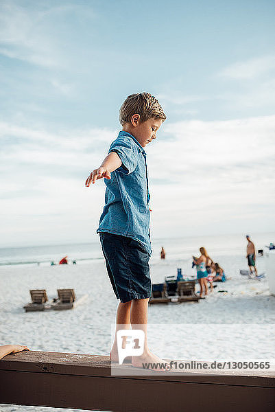 Boy with arms outstretched walking on wooden plank at Panama City Beach against sky